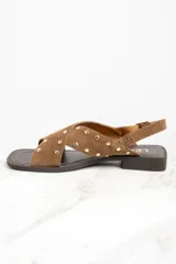 Sandalias bajas de cuero color marrón con tiras cruzadas y tachas doradas.