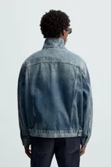 Cazadora de denim de algodón de corte regular, color azul medio lavado. Presenta cuello solapa, manga larga con puños abotonados, dos bolsillos de solapa en el pecho y bolsillos laterales en la costura de la cadera. Cierre frontal con botonadura.