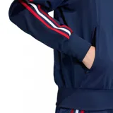 Chaqueta deportiva Adidas Firebird TT C de color azul marino, con cuello alto, cierre frontal y puños y cintura acanalados. Presenta las tres franjas características de Adidas en las mangas, combinando rojo, blanco y azul. El logo del trébol de Adidas se encuentra bordado en dorado en el pecho.