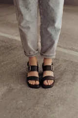 Sandalia de cuero color negro con taco bloque medio y punta cuadrada. Presenta dos tiras anchas sobre el empeine, una de ellas con hebilla metálica dorada, y una tira de sujeción en el talón. Posee base acolchonada para mayor comodidad.