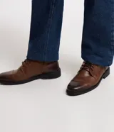 Bota de cuero marrón con caña corta, cierre de cordón y suela negra.