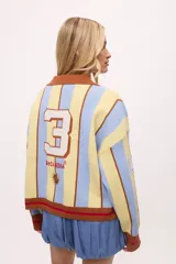 Sweater de punto color crudo con rayas verticales rojas, cuello polo marrón con borde negro, puños y ruedo acanalados en marrón y negro.