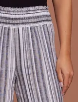 Pantalón de lino con rayas verticales grises y blancas, pretina ancha elastizada en punto smock, pierna ancha y ruedo con tajo.