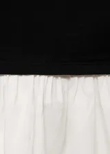 Vestido corto negro con falda blanca, de corte ajustado, con cuello asimétrico y manga larga.