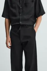 Pantalón negro de corte recto y calce relajado, confeccionado en tejido de algodón con elasticidad. Presenta cintura ajustable con cordón, bolsillos frontales y bolsillos traseros de doble vivo.