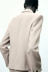 Blazer color beige de corte entallado, con cuello solapa y mangas largas. Tiene bolsillos con solapa en la parte delantera y cierre cruzado con botones.