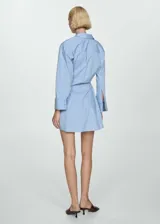 Vestido camisero corto celeste con rayas verticales blancas y marrones, con cierre cruzado y mangas largas con puños abotonados.