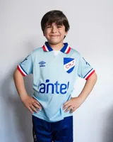 Camiseta de fútbol Umbro del Club Nacional de Football, modelo Alternativa 3 Oficial. Diseño celeste con detalles en azul y rojo en cuello y mangas. Incluye logo de Umbro, escudo del club y sponsor Antel en el frente.