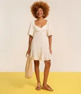 Vestido corto evasê de viscolino color crudo, con escote en V, mangas cortas amplias, recorte cut-out en los laterales de la cintura y volado en el ruedo.