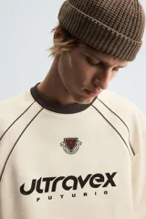 Sudadera color crema de corte relaxed fit, con cuello redondo y manga larga. Presenta un estampado en el frente con la palabra "ULTRAVEX" en letras negras y la palabra "FUTURIO" debajo.