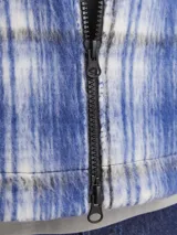 Sobrecamisa corta de manga larga con cuello sport y fit cómodo, confeccionada en tejido plano con efecto lana a cuadros azules y grises. Cuenta con cierre frontal de cremallera, puños con botones, solapa cortaviento, bolsillos en pecho y delanteros.