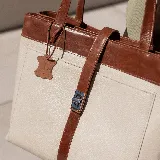 Bolso tipo tote de cuero color marrón con detalles en negro. Tiene doble asa de hombro y correa extraíble regulable. Incluye cierre principal y bolsillo interior.