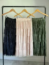 Maxi falda con múltiples capas de flecos, confeccionada en tela elastizada. Disponible en negro, beige y verde militar.