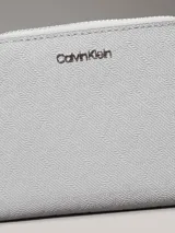 Billetera mediana de color gris claro, con cierre perimetral de cremallera y textura de monograma en relieve. Presenta el logo metálico de Calvin Klein en el frente y tecnología de protección RFID.
