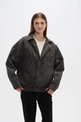 Campera de jean celeste con cuello clásico, solapas, cierre frontal con botones metálicos y mangas largas con puños abotonados. Presenta detalles de costuras diagonales y apliques de tachas metálicas.