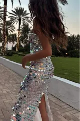 Vestido largo blanco tipo tubo cubierto de lentejuelas tornasoladas y plateadas, con tirantes finos y cierre en la espalda.