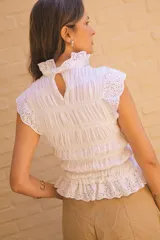 Blusa blanca de algodón con textura fruncida y detalles de broderie en cuello, mangas y ruedo.