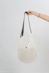Bolso tejido color crudo con textura calada y correa de eco-cuero negra regulable con hebilla metálica.