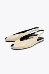 Zapato plano destalonado color beige, con punta abierta, tira trasera con elástico ajustable y suela a contraste de color. Acabado en punta redonda.