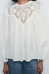 Top blanco de algodón con cuello redondo, manga larga abullonada con elástico y detalle de bordados a tono en el canesú.