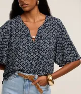 Blusa tipo bata de mangas cortas, confeccionada en viscosa con estampado de follaje en blanco sobre fondo azul marino. Tiene escote en V con detalle de abalorio en el centro.