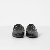 Zapatos tipo mule de cuero negro con punta fina, decorados con tachas plateadas y estrellas metálicas. Tienen un taco bajo y cuadrado.