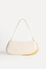 Bolso de hombro alargado color crema, con asa corta y detalle metálico dorado en un lateral. Tiene un bolsillo interior con cremallera y cierre principal con cremallera.
