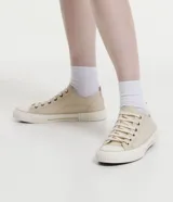 Championes bajos de lona color beige, con puntera redonda, cierre con cordones y suela de goma blanca con detalle de línea en relieve.