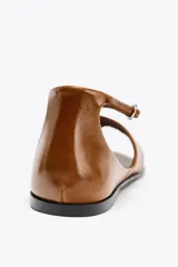 Sandalia plana de piel color marrón caramelo, con tira delantera y tira trasera con cierre de hebilla metálica.