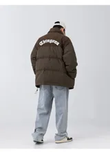 Campera puffer color nude (beige claro) con diseño acolchado. La parte superior de los hombros y el cuello son de pana acanalada. Presenta un bordado en la espalda con la palabra "Chingona" en tipografía gótica blanca. Posee tiras regulables en la cintura.