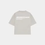 Camiseta beige de corte cuadrado con cuello redondo y estampado blanco en la espalda con el logo de la marca y texto alusivo a sus raíces.