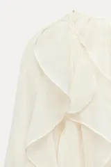 Blusa marrón de gasa con escote en V y manga larga abullonada. Presenta volantes en el mismo tejido y cierre frontal con botones.
