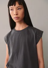 Camiseta gris de algodón con cuello redondo y mangas cortas con tachas plateadas en los hombros.