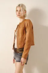 Chaqueta de cuero color marrón claro con detalles de trenzas en cuello, bolsillos y puños. Cierre frontal con ganchos metálicos y forro interior al tono.