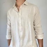 Camisa de lino color beige, de corte oversize, con cuello clásico y mangas largas con puños abotonados.