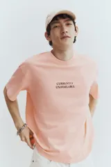 Remera color salmón de corte holgado, cuello redondo y manga corta. Estampado frontal con la frase "Currently Unavailable".