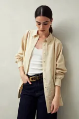 Camisa blanca de lino con botones de nácar, corte recto, cuello clásico y mangas largas con puños abotonados. Presenta detalles de calados tipo vainillas en el frente y las mangas.