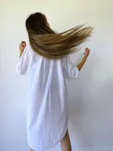 Vestido camisero blanco de corte holgado, con cuello mao, cierre frontal con botones, mangas 3/4 con puños abotonados, dos bolsillos de parche en el pecho y aberturas laterales en el ruedo.