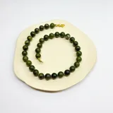 Collar de cuentas esféricas de jade verde, con separadores de hilo lila y cierre de mosquetón dorado.