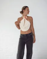 Top color crema o amarillo pálido, estilo halter con cuello atado y escote pronunciado en V con drapeado frontal. El cuello está adornado con una flor de orquídea en tonos amarillo, naranja y rosa.