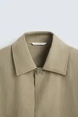 Gabardina color beige de corte recto, con cuello solapa, cierre frontal con botones, bolsillos laterales y puños ajustables con trabilla.