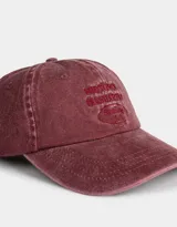 Gorra de béisbol color borgoña, confeccionada en denim con efecto lavado. Presenta bordado frontal con texto y regulador metálico trasero.