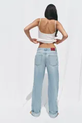 Pantalón de jean celeste de tiro alto, corte recto y largo hasta el tobillo con dobladillo. Tiene cinco bolsillos y cierre frontal cruzado con cremallera y botón.