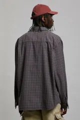Camisa de franela suave a cuadros grises y marrones, de corte holgado, con cuello inglés, tapeta clásica, canesú en la espalda, bolsillo superior abierto, mangas largas con tapeta de manga y puños abotonados, y bajo levemente redondeado.