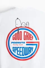 Remera blanca de algodón con cuello redondo y manga corta, corte holgado. Presenta un pequeño estampado en el pecho con el texto "PEANUTS Racing Team" en letras azules y rosadas.
