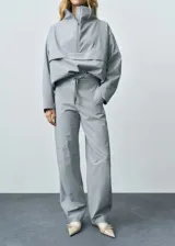 Pantalón largo de tiro medio color gris, estilo jogger, con dos bolsillos laterales, cierre oculto de botón, gancho y cremallera, y forro interior.