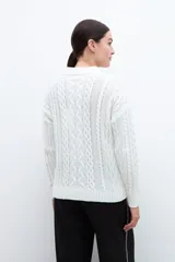 Cardigan crudo de tejido de punto trenzado, con cuello polo, cierre frontal con botones y bolsillos delanteros.