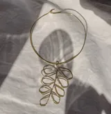 Gargantilla rígida dorada con dije colgante en forma de hoja estilizada.