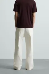 Pantalón negro de algodón con corte relajado y pierna ancha (flare fit). Presenta cierre frontal con botón y cremallera, bolsillos delanteros y bolsillos traseros de plastrón.