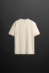 Camiseta color crudo de corte relaxed fit confeccionada en tejido técnico ligero de tacto suave, cuello redondo y manga corta. Tiene un texto estampado en el delantero y detalle de logo estampado en el bajo.